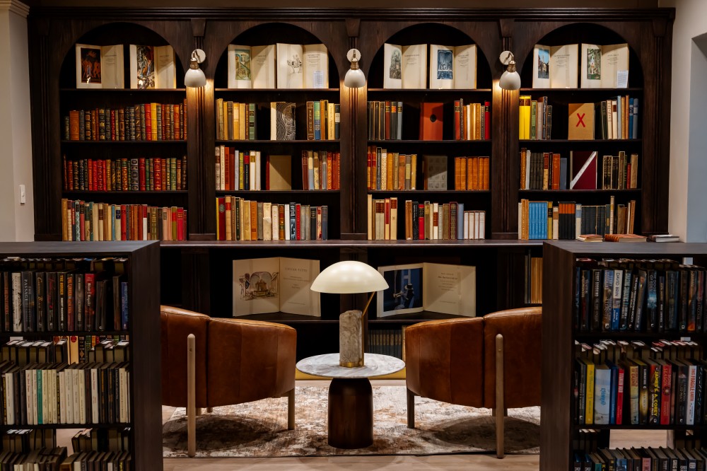 Big dark traditional book shelves filled with books. Two brown leather chairs with a lamp